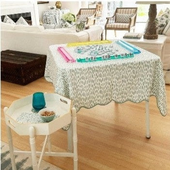 The HOLLY STUART DESIGNS Mahjong and Game Tablecloth in Dash Cadet features a folded white cotton fabric with blue brushstroke pattern, tied with a white ribbon. A stylish accent for any game table or occasion from HOLLY STUART DESIGNS.