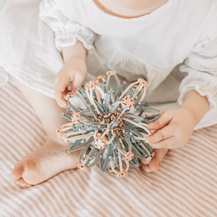 A child sitting on a striped blanket, holding a colorful Mindfulness Magic Ball, promoting mindful play and relaxation.