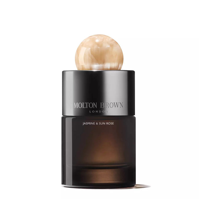 A bottle of MOLTON BROWN JASMINE AND SUN ROSE EAU DE PARFUM stands with a dark translucent base, shiny black cap, and round marble-like beige top against a plain white background.