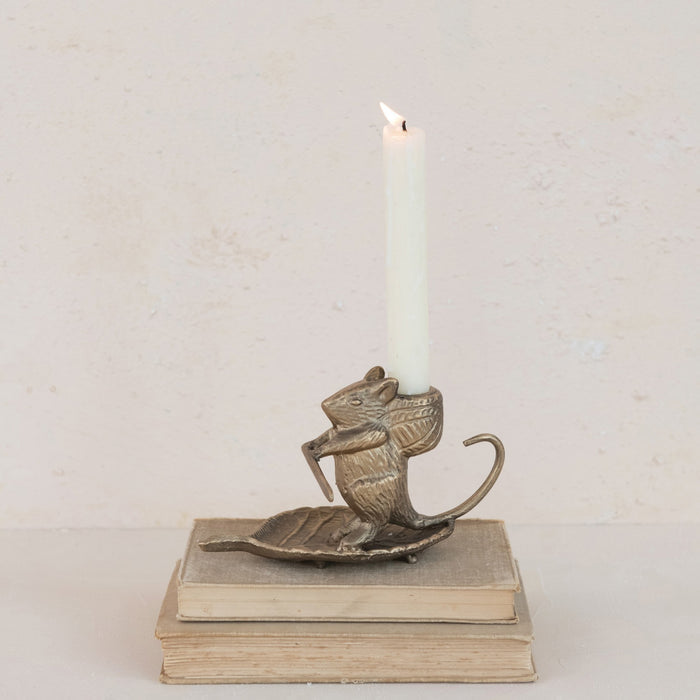 The CREATIVE COOP MOUSE ON LEAF CAST METAL TAPER HOLDER features an antique gold finish, measures 6"L x 3.25"H, and has a curled tail while sitting on a leaf-shaped base. Shown on a white background.