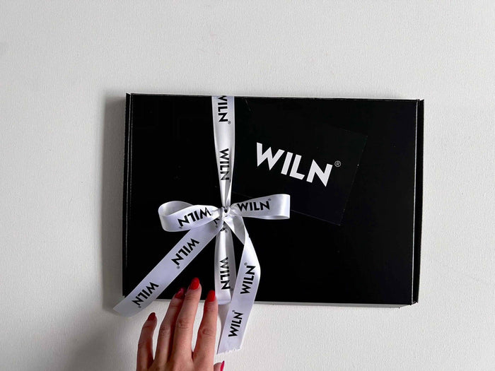 A hand presenting a black gift box tied with a white ribbon branded 'WILN', showcasing elegant packaging.