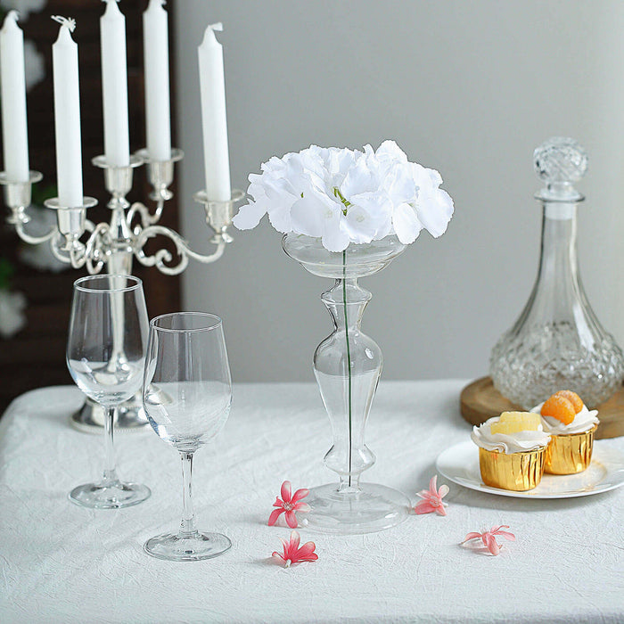 Elegant glass vase with white flowers, candles, and desserts on a table.