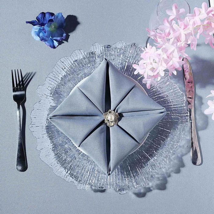 Elegant gray napkin folded with a brooch on a clear glass plate with flowers.