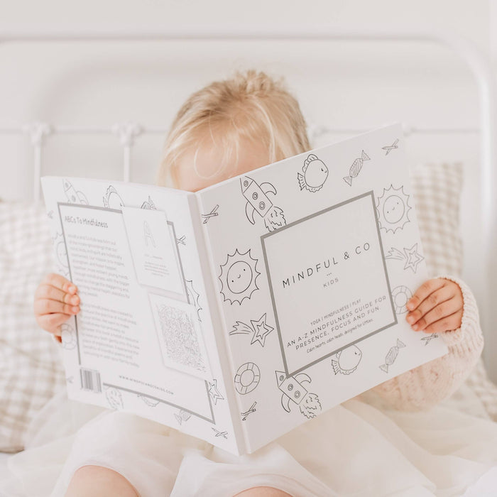 Child holding a coloring book with 'Mindful & Co' on a soft surface