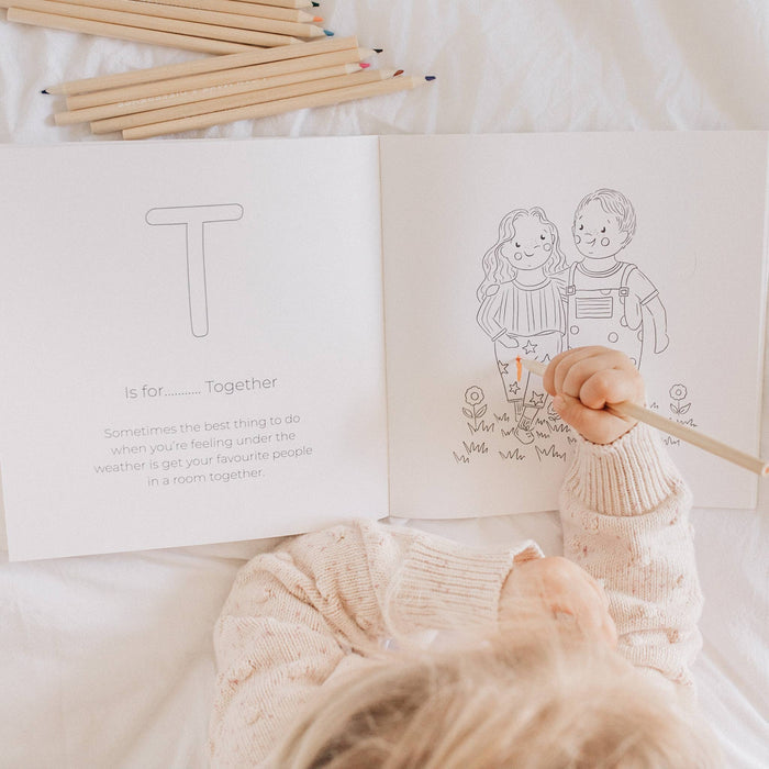 Child coloring a picture of two children together in a book with wooden crayons.