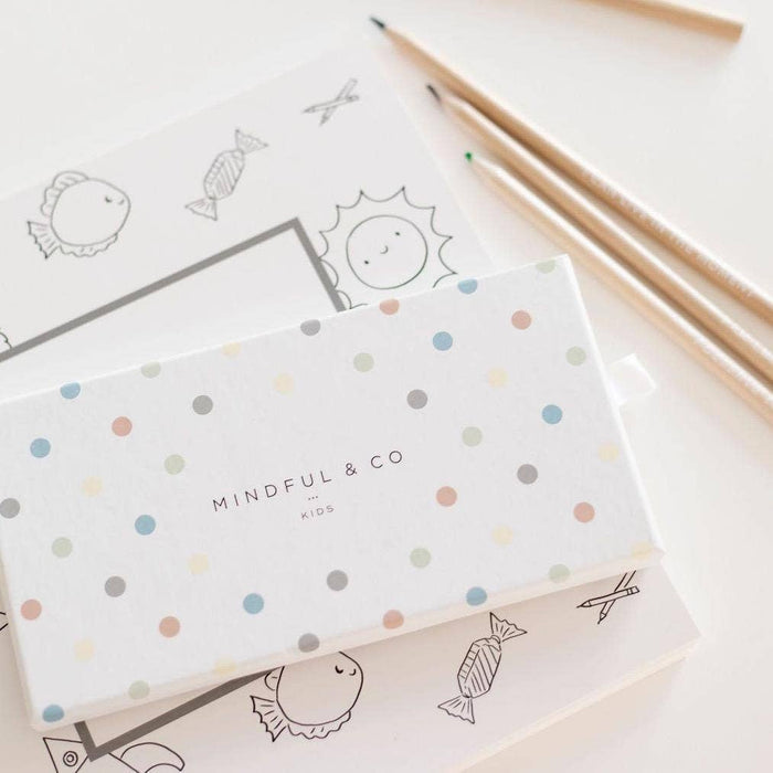 Affirmation Colouring Pencils set packaging with playful dots, lying on coloring sheets designed for kids.