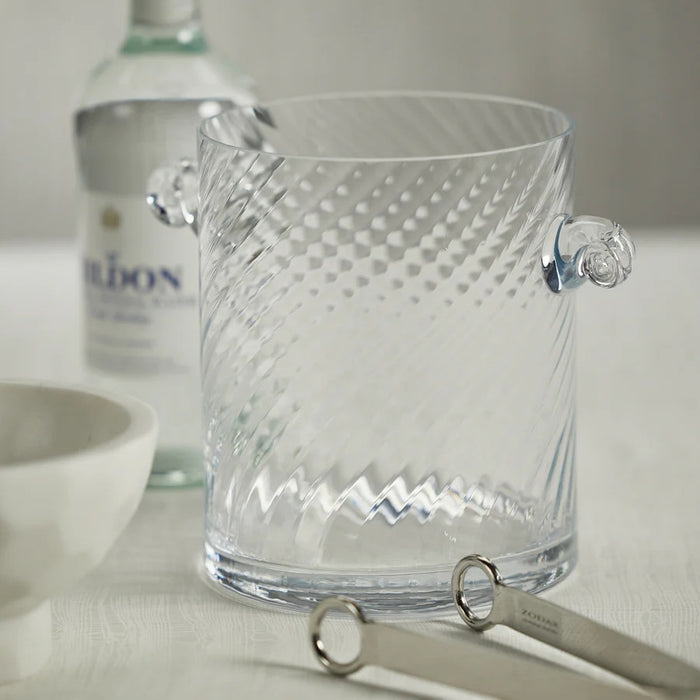 The BAGATELLE SWIRL GLASS ICE BUCKET by ZODAX features a clear, textured spiral design with diagonal swirls and two round handles—a modern bar accessory shown on a white background.