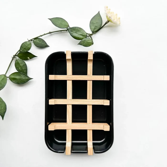 Black rectangular tray with wooden grid on a white background with green leaves.