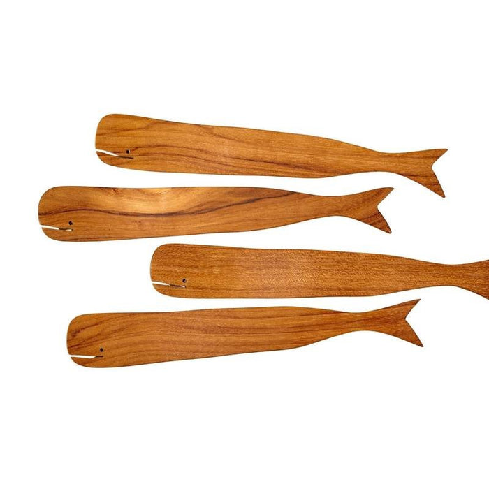 The BE HOME - TEAK WHALE SPREADERS by BE HOME, INC rest on a round white marble cutting board with a hole at the top, displayed on a wooden surface.