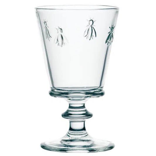 The LA ROCHERE BEE WATER GLASS, with its embossed Napoleonic bee, rests on a sunlit table beside a green lime drink, fresh cantaloupe slices, and white flowers for an effortlessly elegant display.