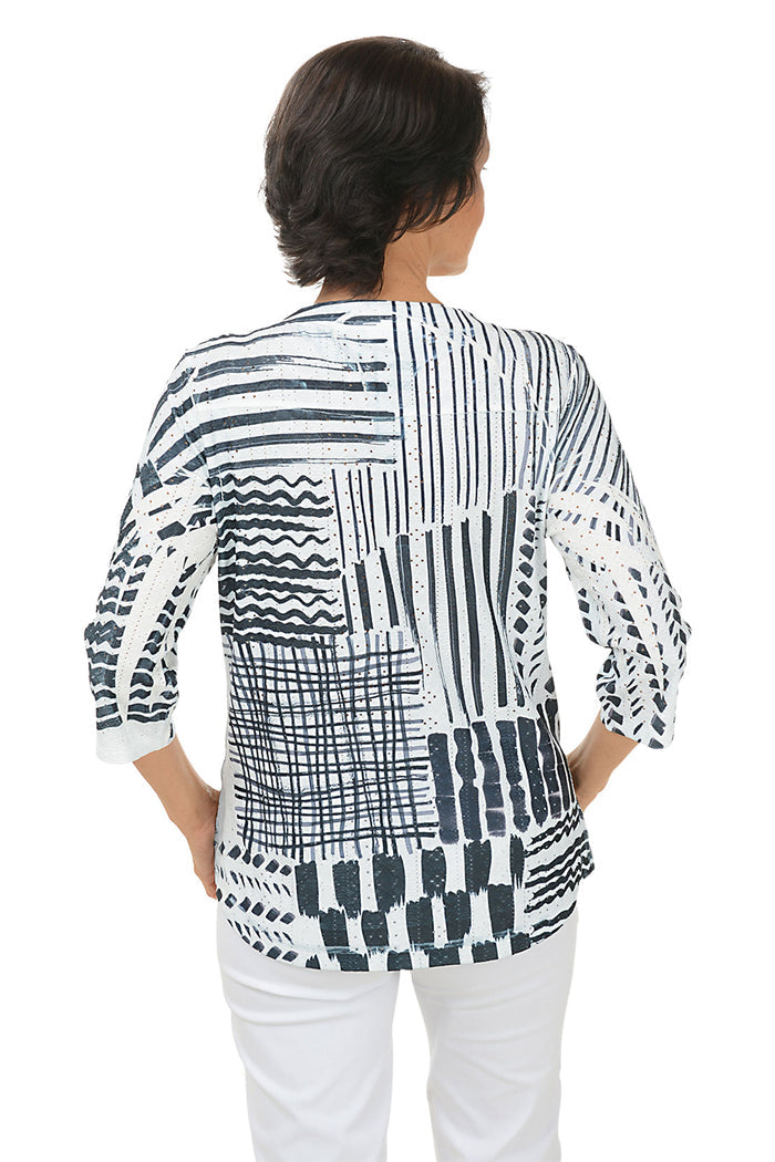 Woman wearing a 3/4 sleeve black and white patterned blouse with white pants on a white background. Back shot.