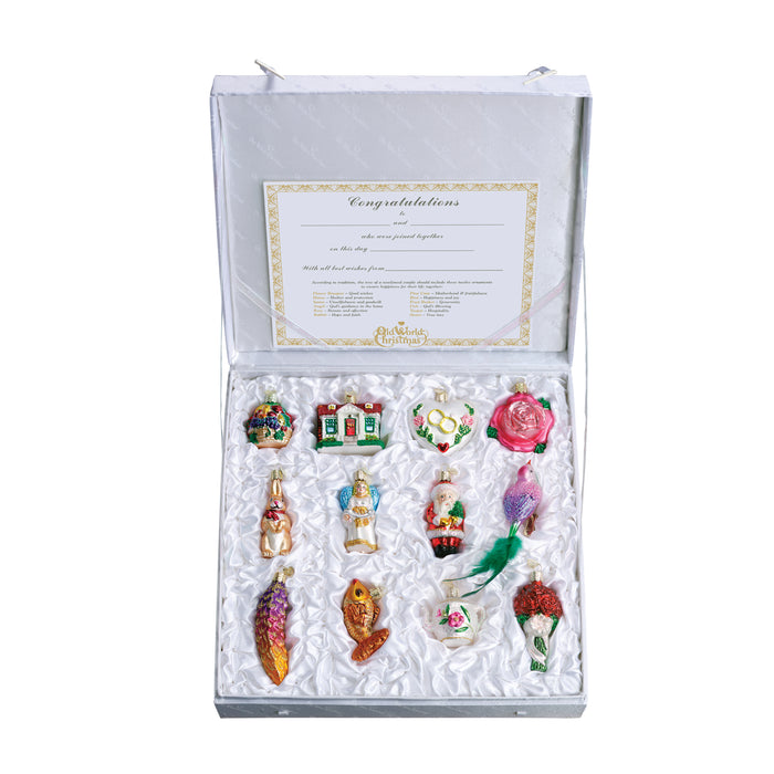 A decorative gift box with a satin lining displays twelve colorful, assorted glass Christmas ornaments, each shaped like different objects or figures, arranged neatly in rows. A congratulatory card is attached inside the lid.
