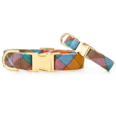 The BUCHANAN PLAID DOG COLLAR by THE FOGGY DOG features a colorful flannel design with gold metal hardware, including a D-ring and a buckle, shown on a white background.