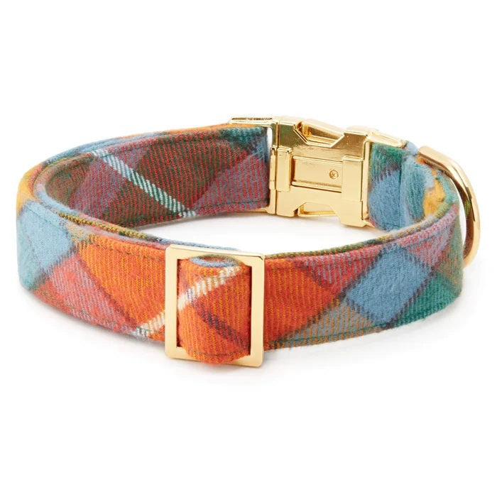 The BUCHANAN PLAID DOG COLLAR by THE FOGGY DOG features a colorful flannel design with gold metal hardware, including a D-ring and a buckle, shown on a white background.