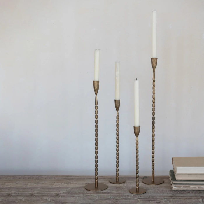 The CREATIVE COOP CAST IRON TAPER HOLDER IN BRASS FINISH, LARGE, features a tall, slender design with a textured segmented stem and round base, perfect for displaying a single taper candle.