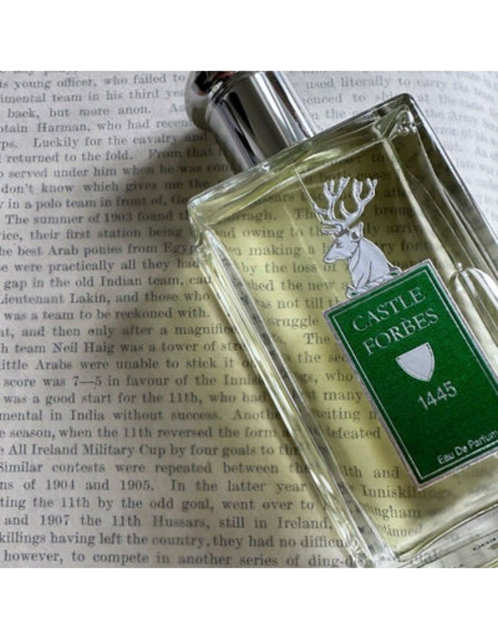 A clear glass bottle with a green label reading 'CASTLE FORBES 1445' and a white deer emblem, placed on top of an open book with printed text.