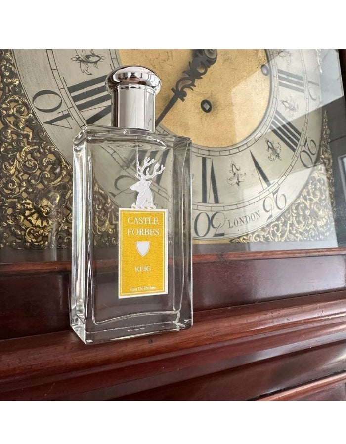 Castle Forbes Keig Eau de Parfum bottle on a wooden mantel in front of an antique clock, elegant citrus fragrance hero shot