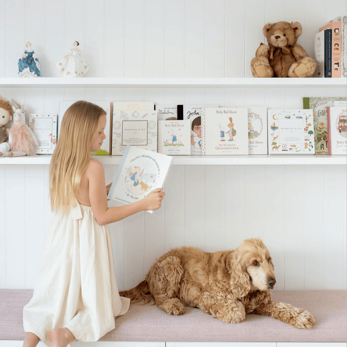 A girl reading Charlie's Mindful Adventures By The Sea to a dog on a cozy shelf with children's books.