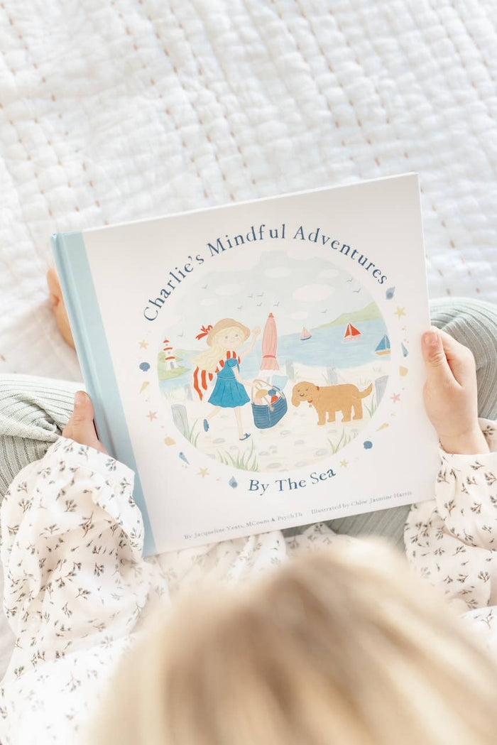 Child holding Charlie's Mindful Adventures By The Sea book, promoting mindfulness and seaside adventure for young readers.