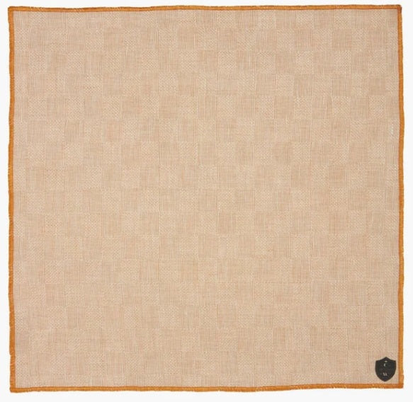 The CLIFTON WILSON - TAN CHECK LINEN POCKET SQUARE features a subtle check pattern, orange edging, and a small black shield emblem in one corner.