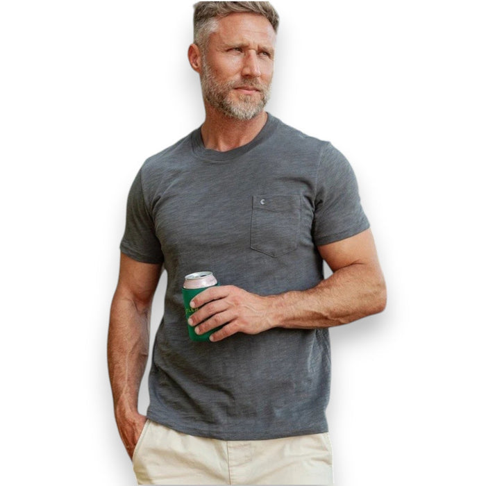 A man with a gray beard wearing the CRIQUET - SLUB COTTON SHORT SLEEVE POCKET T-SHIRT IN WASHED BLACK holds a canned drink in a green koozie outdoors, with trees and a white vehicle blurred in the background.