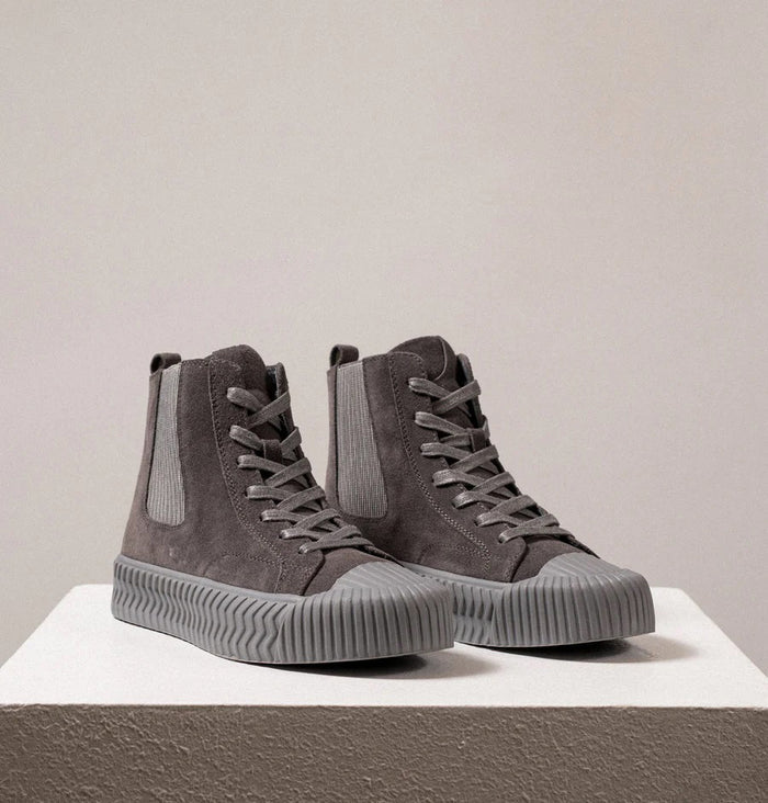 The DANIELLA LEHAVI - OSAKA HIGH TOP SNEAKER by DANIELLA LEHAVI features gray suede uppers and ribbed rubber soles, shown on a white pedestal against a plain light background. These stylish high-tops perfectly combine everyday comfort with modern style.