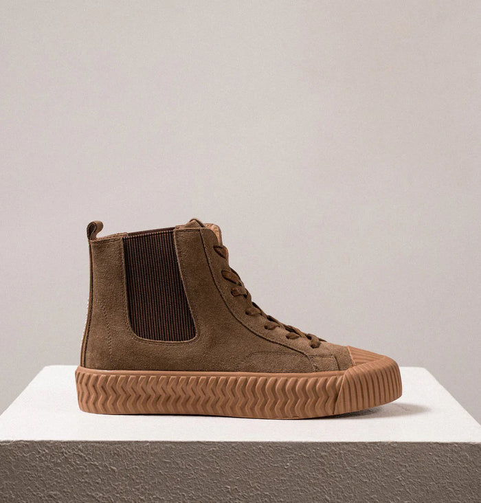 The DANIELLA LEHAVI - OSAKA HIGH TOP SNEAKER features brown suede, tan ribbed rubber soles, and side elastic panels—a stylish and comfy choice from DANIELLA LEHAVI, shown on a white pedestal against a neutral background.
