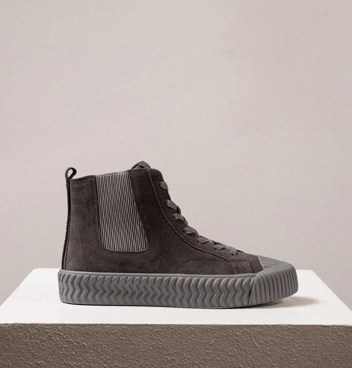 The DANIELLA LEHAVI - OSAKA HIGH TOP SNEAKER by DANIELLA LEHAVI features gray suede uppers and ribbed rubber soles, shown on a white pedestal against a plain light background. These stylish high-tops perfectly combine everyday comfort with modern style.