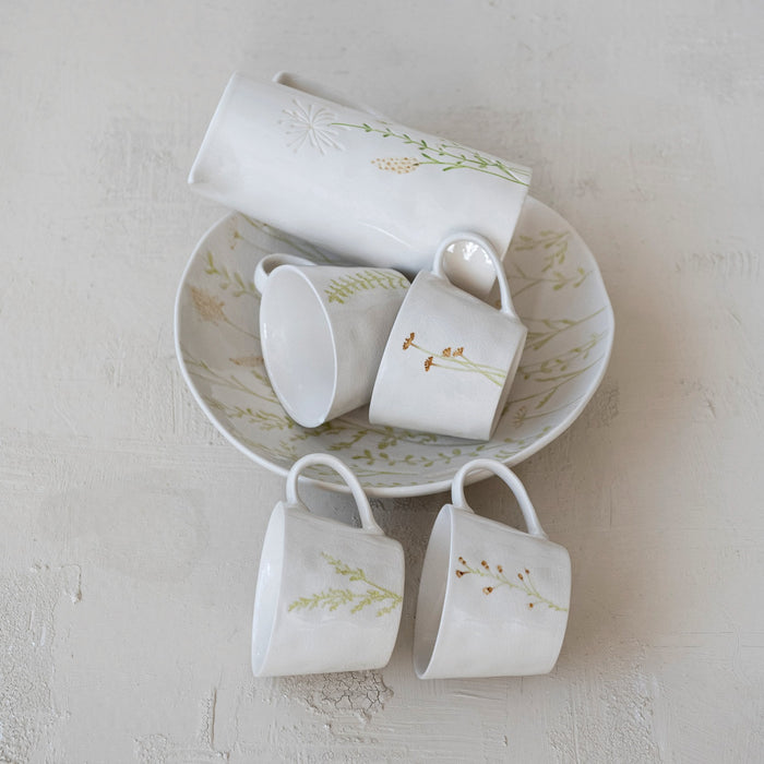 Four DEBOSSED STONEWARE MUGS WITH BOTANICAL PATTERN by CREATIVE COOP, featuring cream color, unique green botanical designs, and a subtle reactive glaze finish, are lined up side by side on a white background.