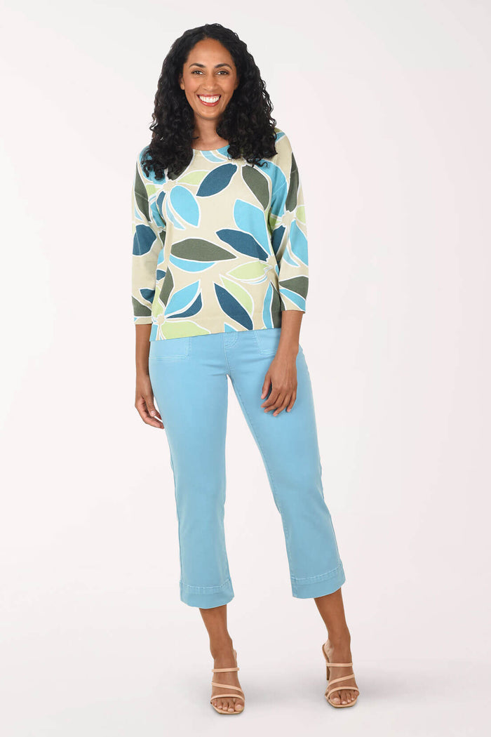 Woman wearing a patterned top and light blue pants on a white background