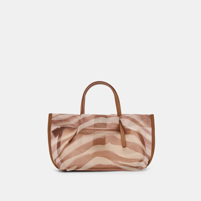 A woman in a light blazer and dress sits on a boat, sunlight highlighting her look and the DOLCE VITA - SELENE ZEBRA MESH BAG resting on her knee. The bright, relaxed scene showcases the stylish bag from DOLCE VITA.