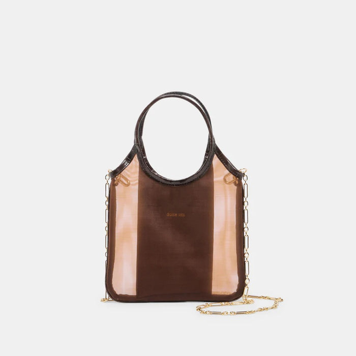 A person in a textured, light dress holds the DOLCE VITA - SYLVENE Crossbody Mesh Bag in Chocolate. A smartphone is visible inside, and a gold keychain decorates the round handle.