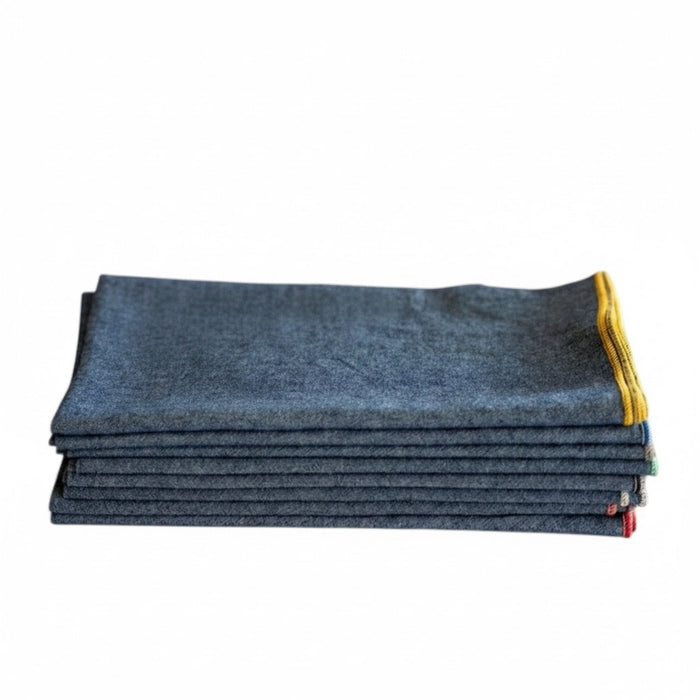 A woven wooden basket displays DOT AND ARMY Chambray Cocktail Napkins—each gray napkin features a different brightly colored stitched edge—all set against a white background.