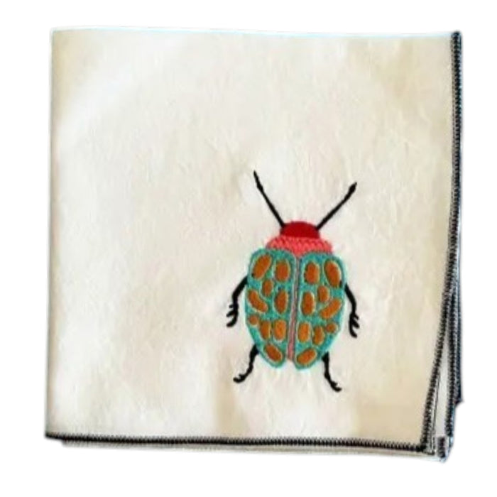 The DOT AND ARMY - EMBROIDERED BEETLE TOWEL by DOT AND ARMY is a neatly folded white cotton kitchen towel with black trim, embroidered with a colorful beetle featuring a red head and turquoise body with orange spots.