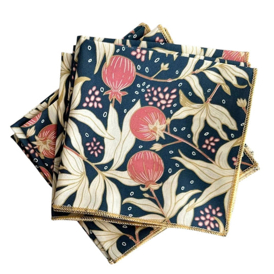 The DOT AND ARMY Gooseberry Cocktail Napkin features a red, cream, and dark green floral and pomegranate print with yellow-stitched edges—sustainable napkins ideal for any gathering.
