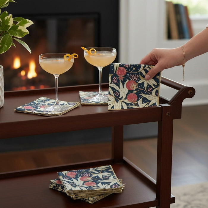 The DOT AND ARMY Gooseberry Cocktail Napkin features a red, cream, and dark green floral and pomegranate print with yellow-stitched edges—sustainable napkins ideal for any gathering.