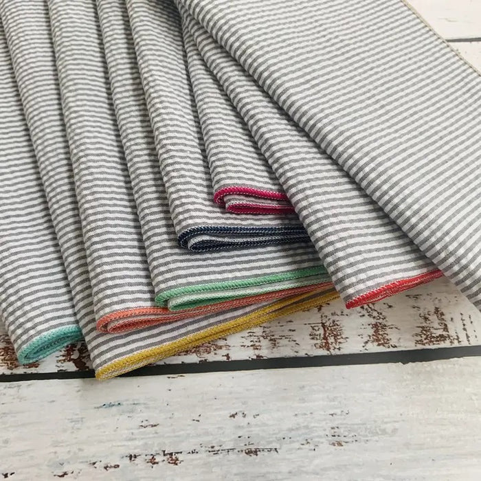 A set of DOT AND ARMY - GREY SEERSUCKER DINNER NAPKINS, each with colorful edging, is fanned out on a white background.