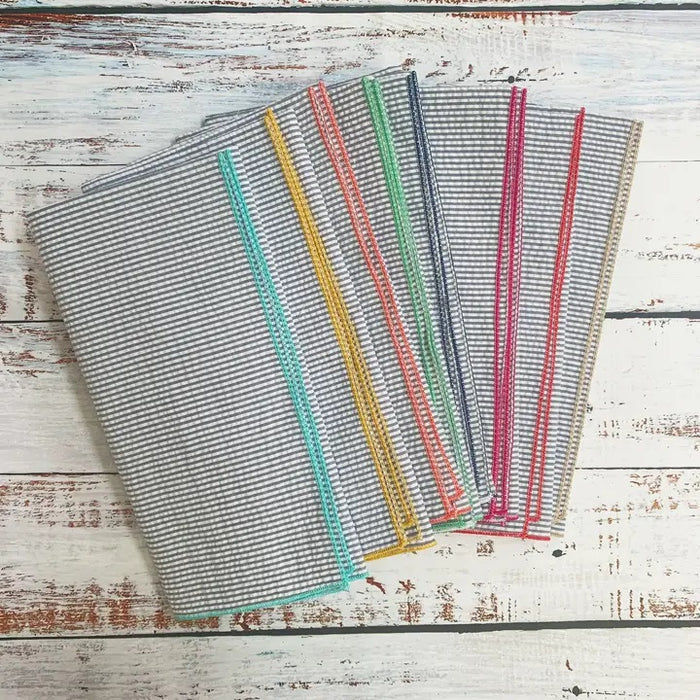 A set of DOT AND ARMY - GREY SEERSUCKER DINNER NAPKINS, each with colorful edging, is fanned out on a white background.