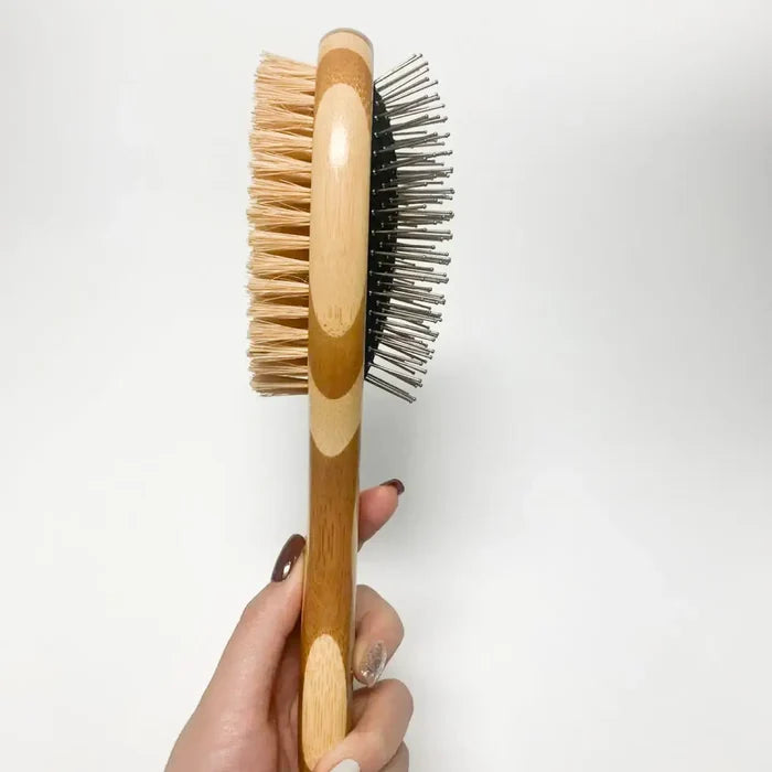Hand holding a wooden hairbrush with bristle and rubberized back on a white background