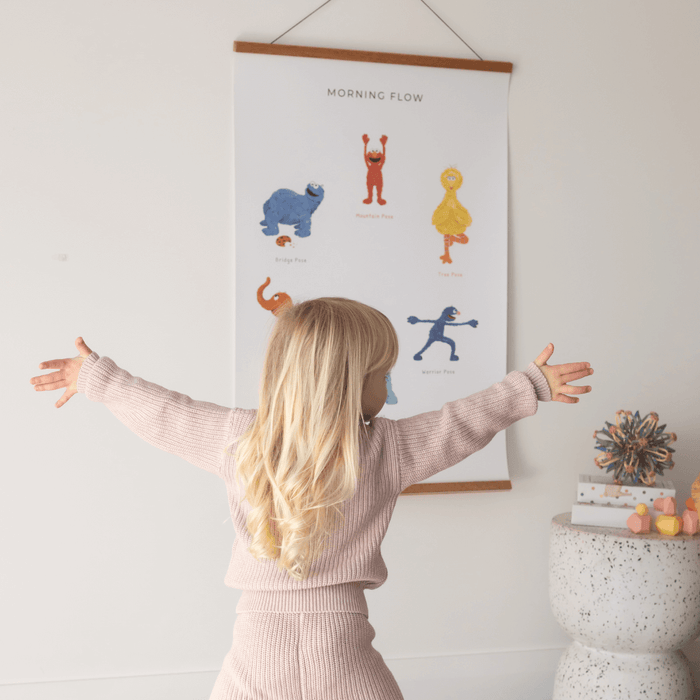 Child practicing yoga poses from the Double-sided Sesame Street Yoga Poses Print in a bright room.