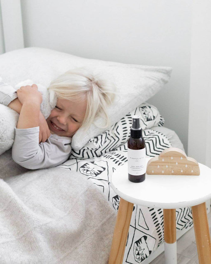 Aromatherapy Spray placed on a table beside a joyful child snuggled in bed, promoting restful sleep.