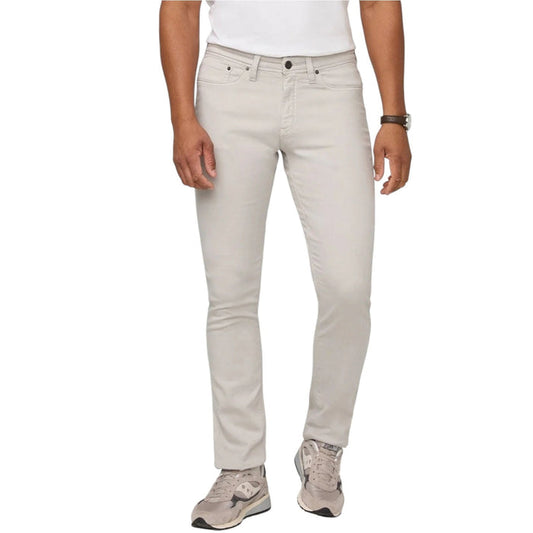 A person stands facing forward on a plain light background, wearing DUER NO SWEAT ATHLETIC TAPER PANTS IN MIST and matching light gray sneakers, feet slightly apart.