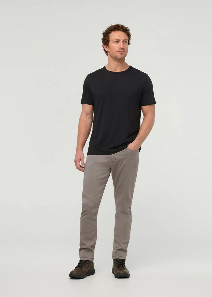 Close-up of the back of a person wearing DUER No Sweat Athletic Taper Pants in Stone, featuring two back pockets and a tan leather DUER patch on the waistband. They're also wearing a black shirt.
