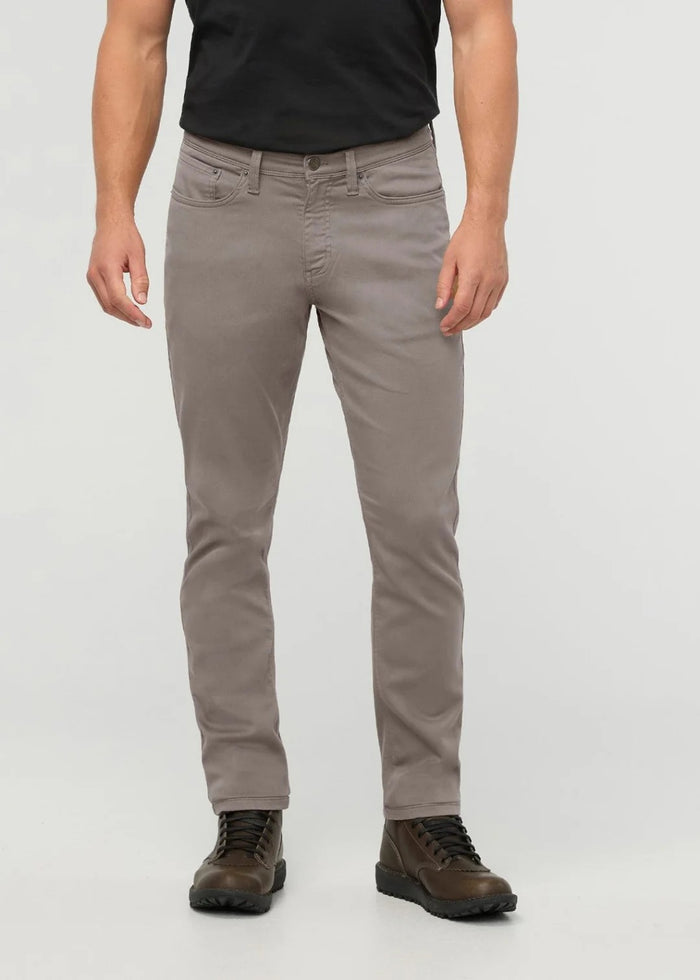 Close-up of the back of a person wearing DUER No Sweat Athletic Taper Pants in Stone, featuring two back pockets and a tan leather DUER patch on the waistband. They're also wearing a black shirt.