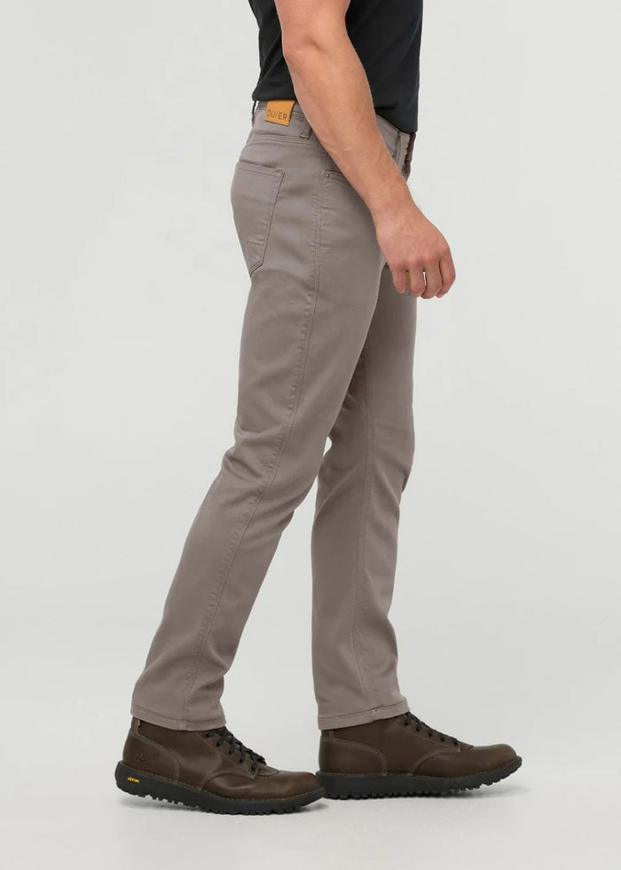 Close-up of the back of a person wearing DUER No Sweat Athletic Taper Pants in Stone, featuring two back pockets and a tan leather DUER patch on the waistband. They're also wearing a black shirt.