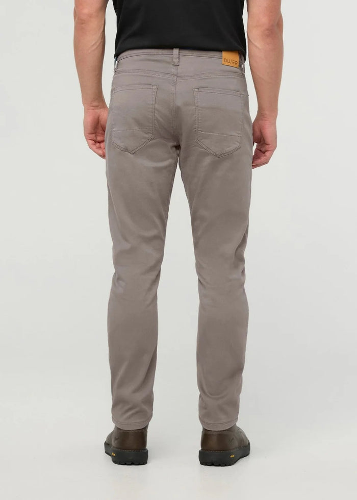 Close-up of the back of a person wearing DUER No Sweat Athletic Taper Pants in Stone, featuring two back pockets and a tan leather DUER patch on the waistband. They're also wearing a black shirt.