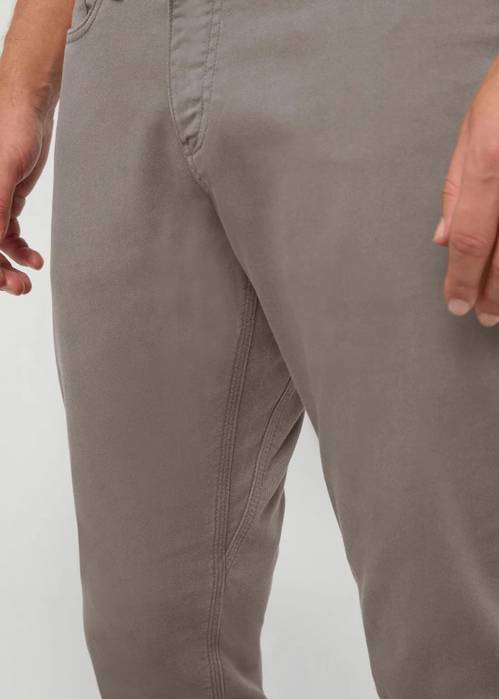 Close-up of the back of a person wearing DUER No Sweat Athletic Taper Pants in Stone, featuring two back pockets and a tan leather DUER patch on the waistband. They're also wearing a black shirt.