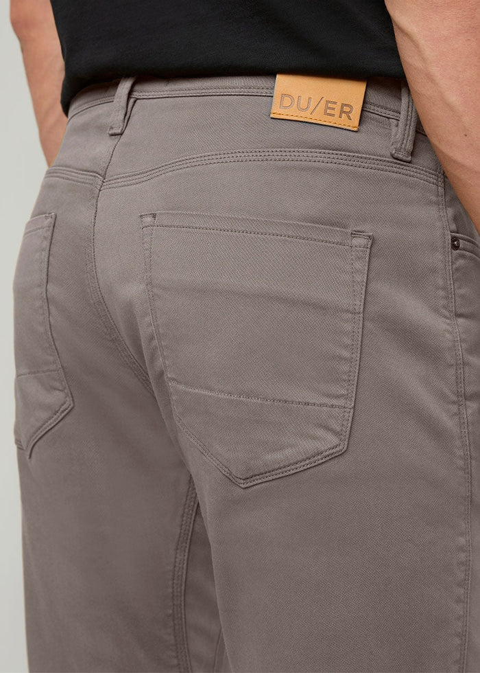 Close-up of the back of a person wearing DUER No Sweat Athletic Taper Pants in Stone, featuring two back pockets and a tan leather DUER patch on the waistband. They're also wearing a black shirt.
