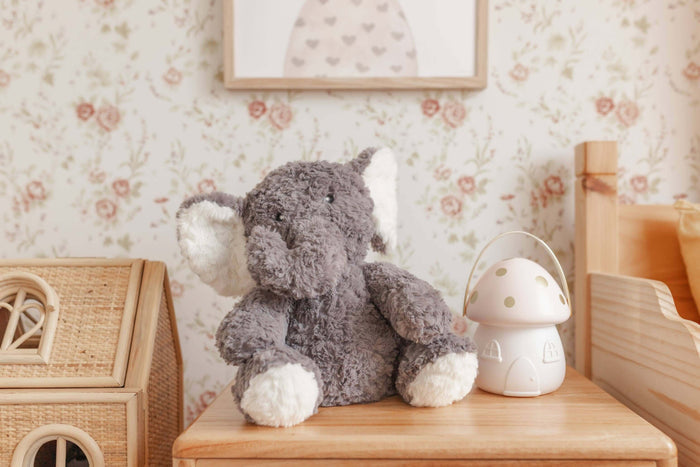 Eleanor The Weighted Elephant plush toy sitting on a wooden table in a cozy room decor.