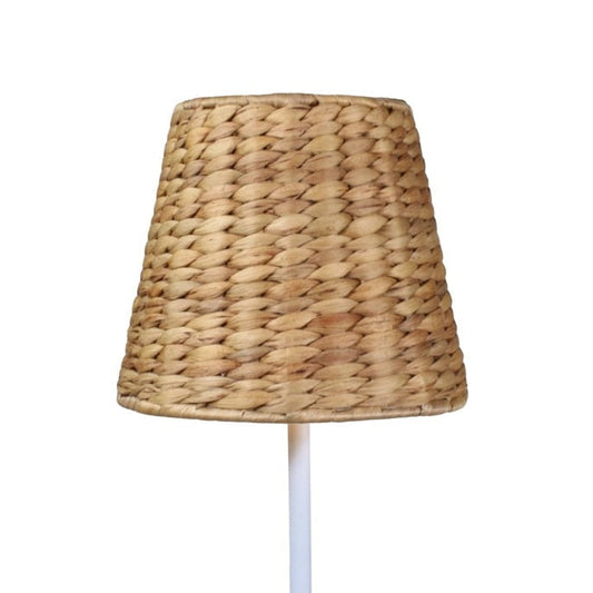 A modern poolside area features white lounge chairs, a potted fern, EMPIRE Water Hyacinth Woven Wicker Shade XXL by Zafferano America, white swan float, and a cordless lamp with glass water bottle on the table.